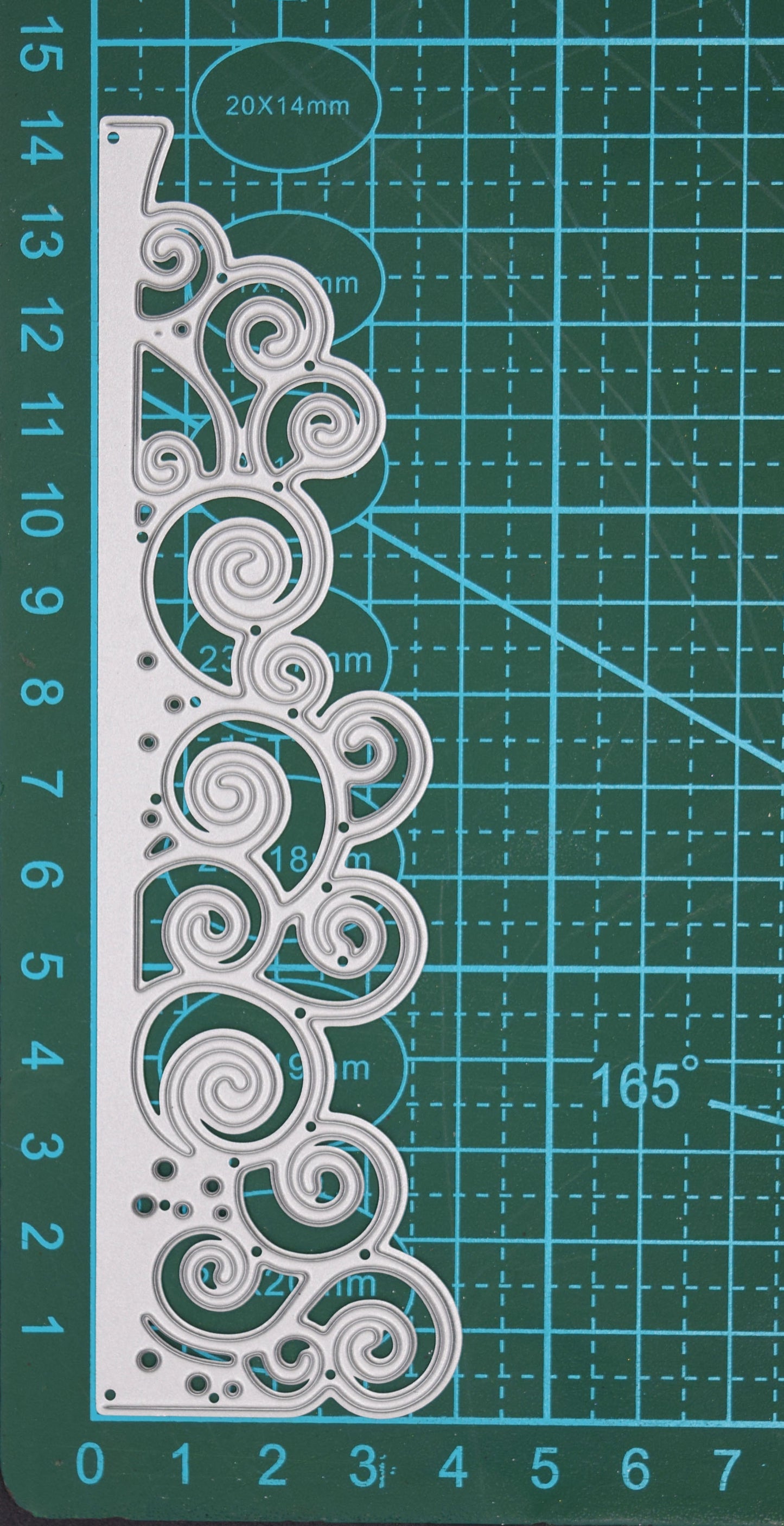 Swirly waves border metal cutting die shown vertically on a centimetre cutting mat for scale