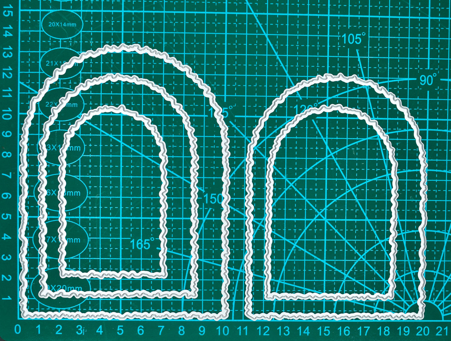 Torn edge arch metal cutting dies shown on a measurement mat, with the nesting set beside a larger arch die for size comparison.