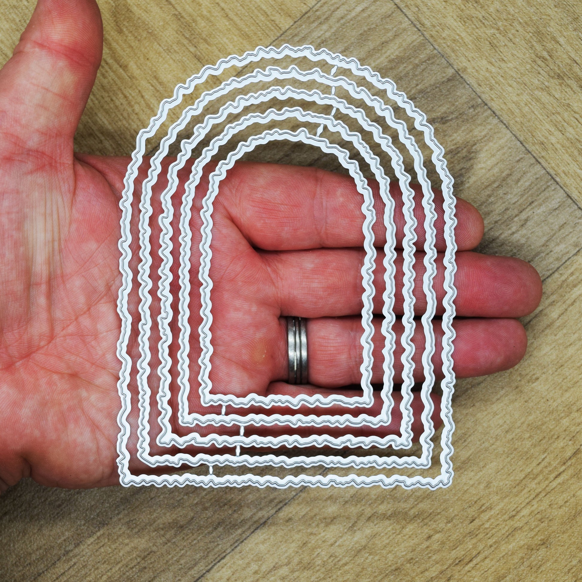 Five-piece torn edge arch metal cutting die set held in a hand to show scale for card making and papercraft.