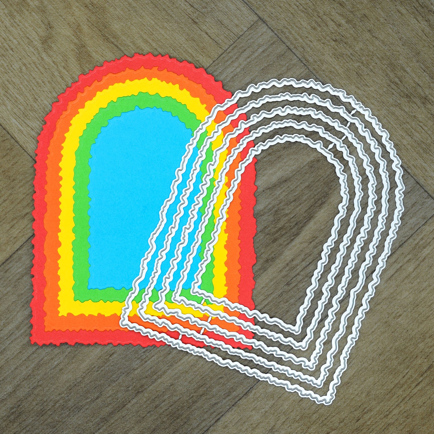 Torn edge arch nesting metal cutting dies placed over bright layered cardstock cuts to show the graduated sizes and cut shape.
