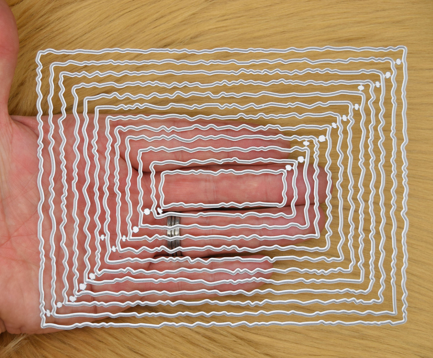 Twelve graduated torn edge rectangle metal cutting dies held in hand to demonstrate the overall size of the nesting set