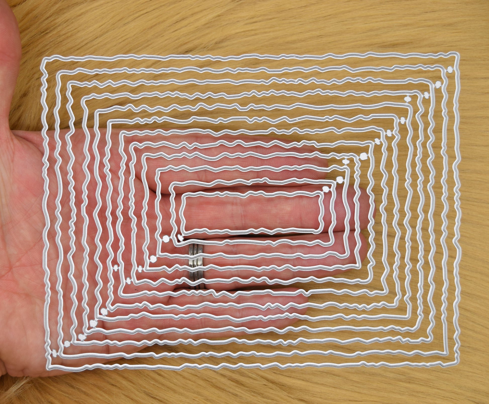 Twelve graduated torn edge rectangle metal cutting dies held in hand to demonstrate the overall size of the nesting set