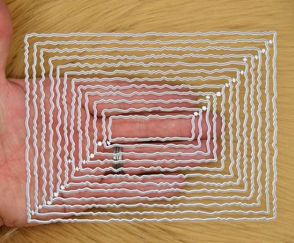 Twelve graduated torn edge rectangle metal cutting dies held in hand to demonstrate the overall size of the nesting set