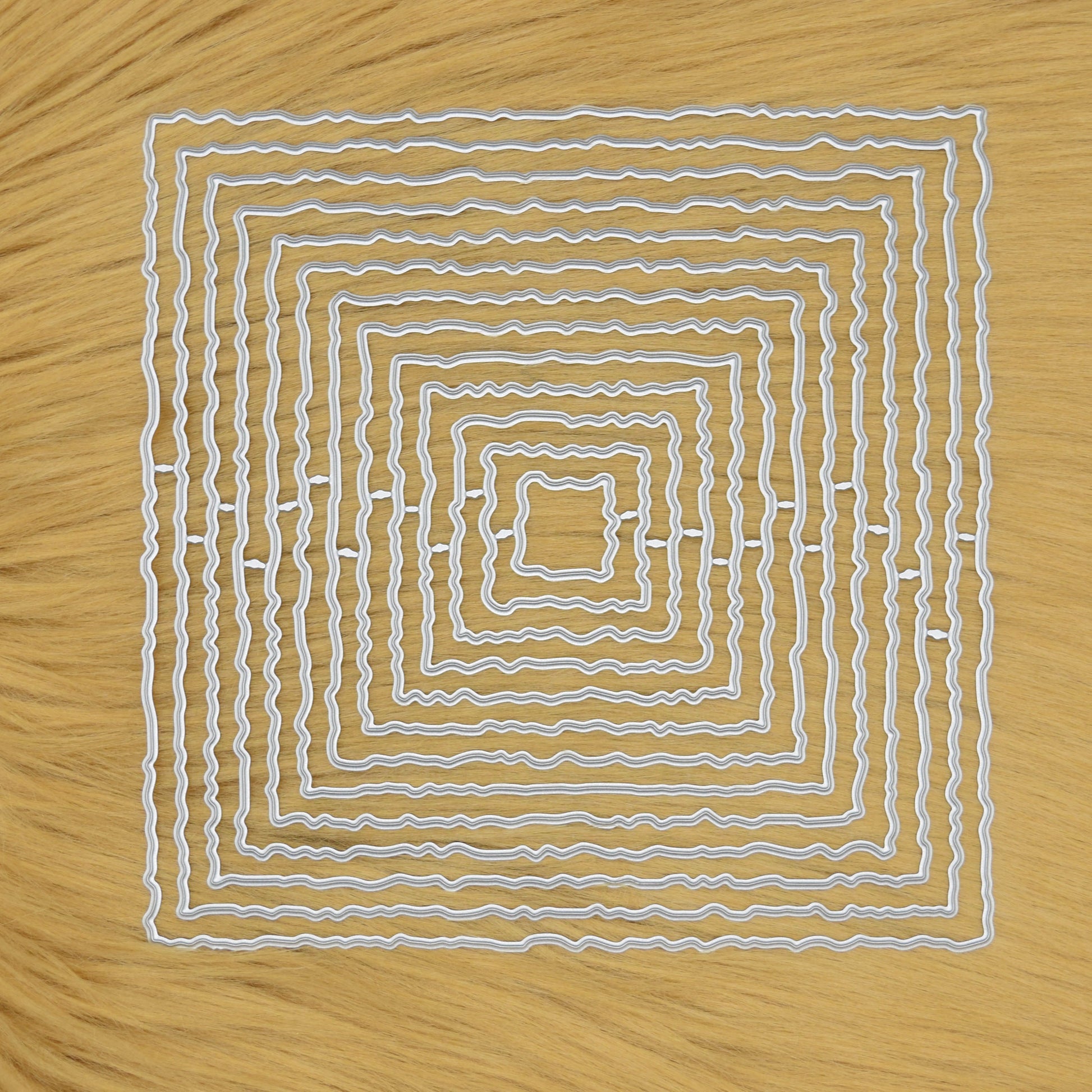 Set of thirteen torn edge square nesting metal cutting dies arranged on a faux fur  background