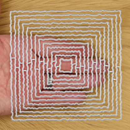 Thirteen graduated torn edge square metal cutting dies held in hand to demonstrate the overall size of the nesting set