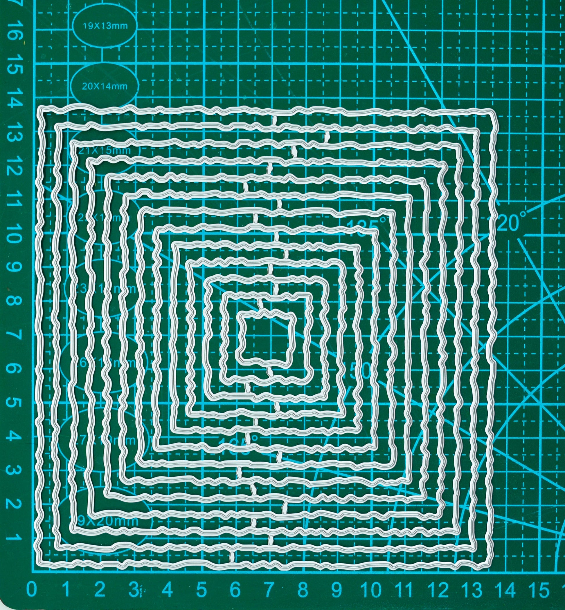 Set of thirteen graduated torn edge square nesting metal cutting dies displayed on a centimetre cutting mat