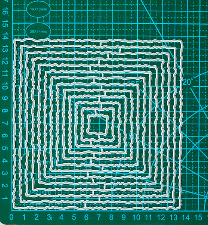 Set of thirteen graduated torn edge square nesting metal cutting dies displayed on a centimetre cutting mat