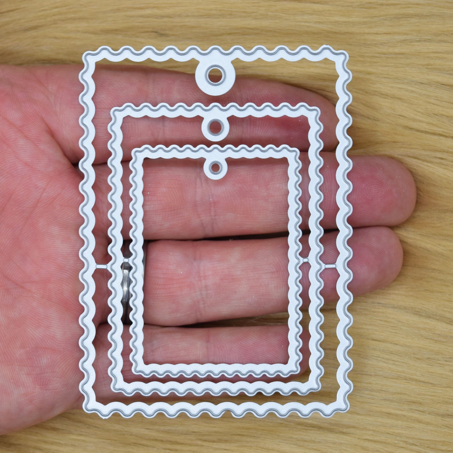 Wavy tag nesting metal cutting dies shown in hand for scale